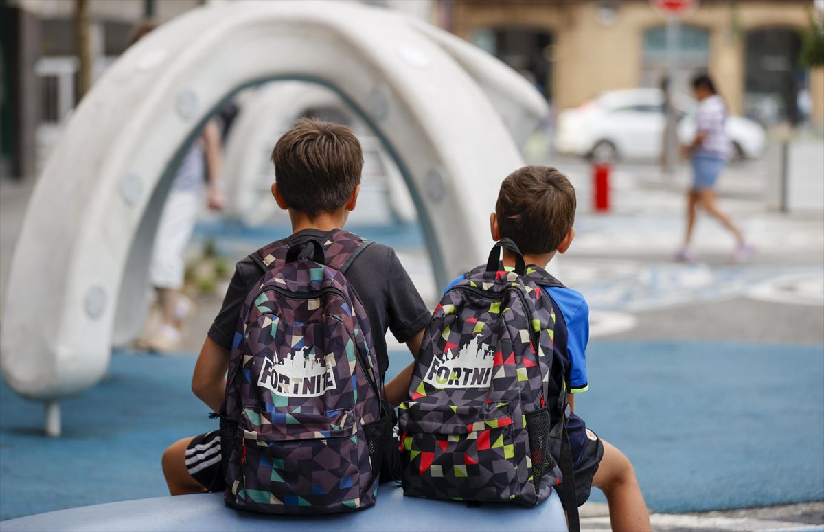 Dos menores con mochilas de clase