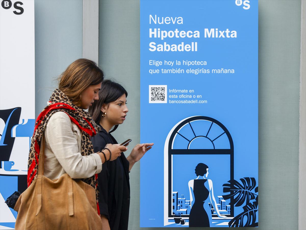 Dos personas pasan frente a una sucursal bancaria con propaganda de una hipoteca mixta. Foto: EFE