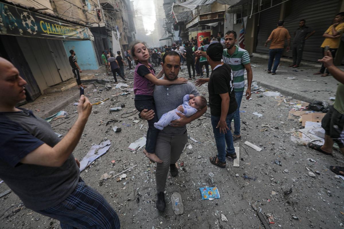Un gazatí huye con niños en brazos tras el ataque al campamento de refugiados Al-Shati. Foto: EFE. 