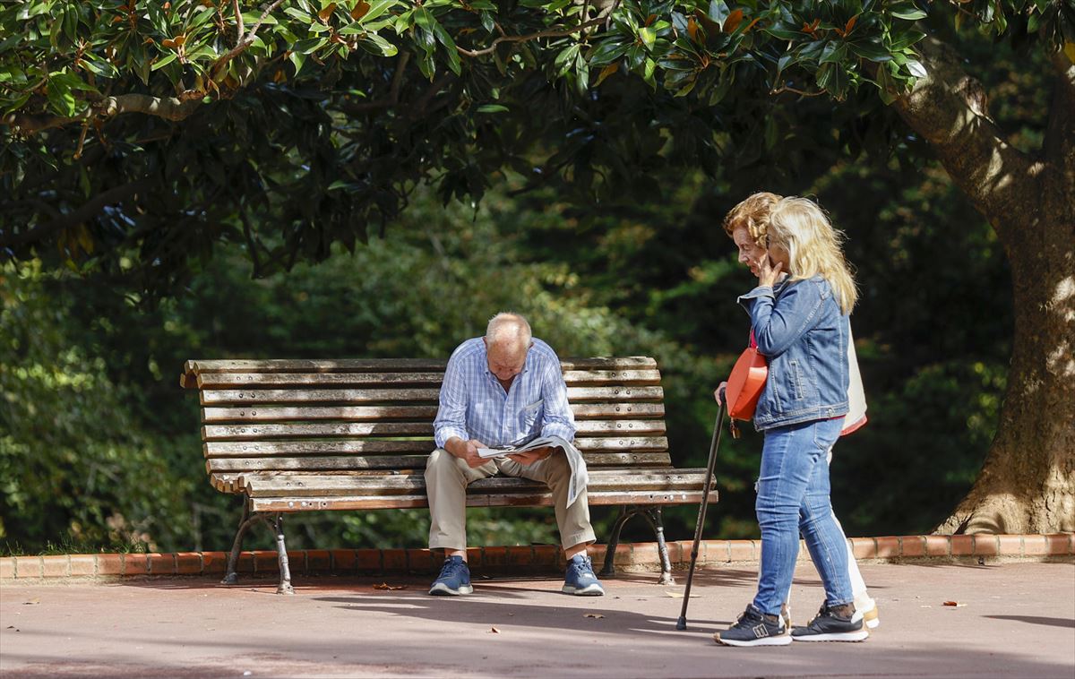 Un jubilado sentado en un banco y una jubilada paseando